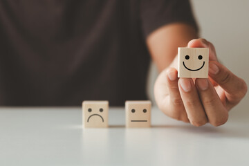 Customer satisfaction concept.  Hand of a businessman chooses a smiling face on a wooden cube...