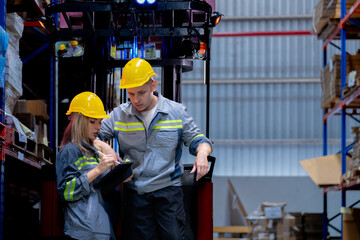 Two male and female factory checkers are discussing work on a warehouse truck. While working in a warehouse for industrial products