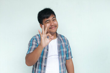 Excited and happy young Asian man gives thumbs up or ok sign hand gesture of approval, isolated by...