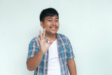 Excited and happy young Asian man gives thumbs up or ok sign hand gesture of approval, isolated by...