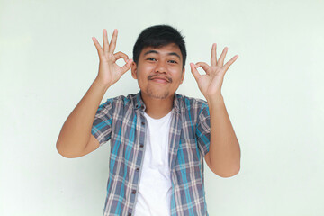 Excited and happy young Asian man gives thumbs up or ok sign hand gesture of approval, isolated by...