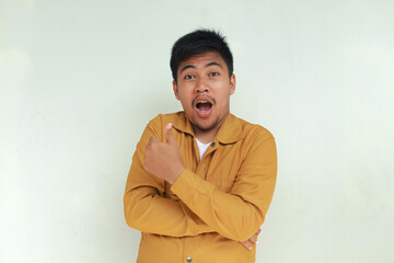 Excited and happy Asian man gives thumbs up hand gesture of approval, isolated by gray background.