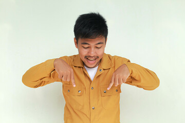 Excited and happy Asian man pointing at the copy space below him, isolated by gray background.