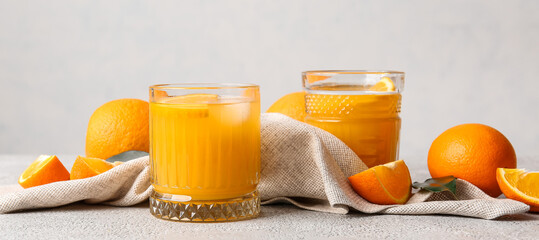 Glasses of tasty orange juice on light background