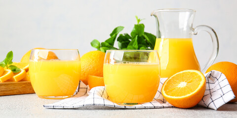 Glasses of tasty orange juice on light background