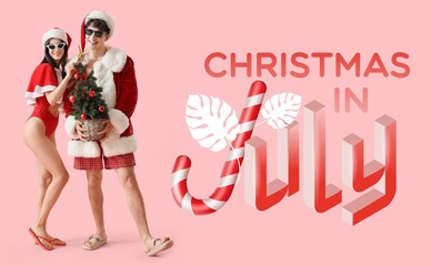 Young couple in Santa costumes and with fir tree on pink background. Christmas in July