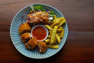 Chicken cordon bleu with crinkle cut fries and vegetable salad, served on striped blue plate, over wooden table, cafe environment
