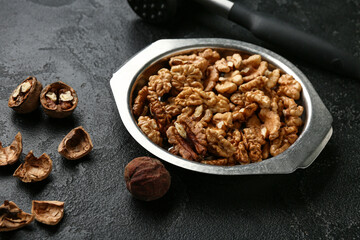 Metal bowl of tasty walnuts on black background