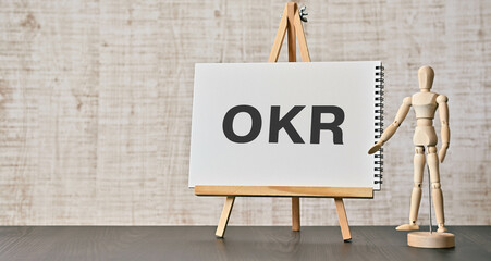There is wood cube with the word OKR. It is an abbreviation for Objectives Key Results as...