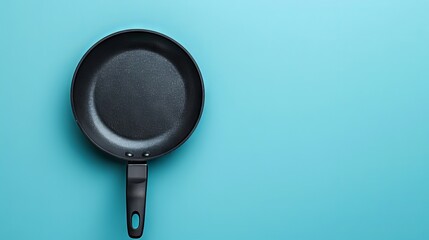 Top view of a black frying pan with a handle placed on a blue background, ideal for kitchen and cooking-themed designs and advertisements.