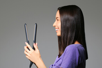 Obraz premium Beautiful young woman with hair straightener on light background