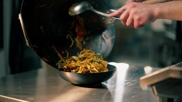 close-up in professional kitchen the chef cooks and pours wog noodles with vegetables into a deep plate