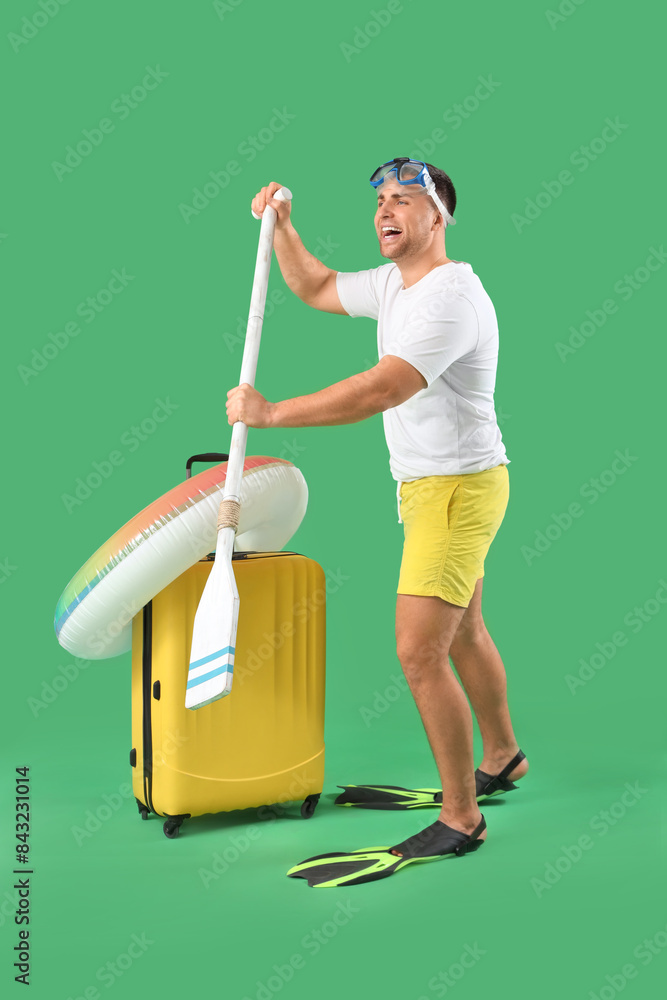 Poster Male tourist with suitcase and swimming accessories on green background