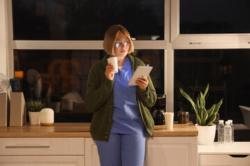 Female nurse with tablet computer and coffee cup at hospital in evening