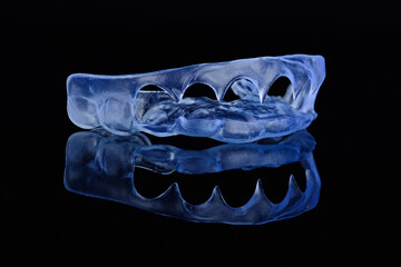 Printed transparent dental cap made of polymer on a light colorful background. Dental splint against bruxism.