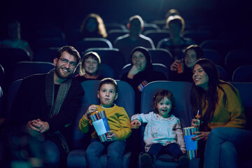 A modern family enjoys quality time together at the cinema, indulging in popcorn while watching a movie with their children