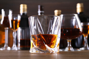 Different delicious liqueurs in glasses and bottles on wooden table, closeup
