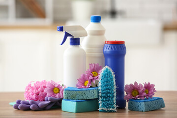 Set of cleaning supplies and spring flowers on wooden table in kitchen