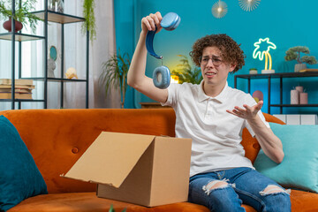 Unhappy young Caucasian man guy unpacking carton box, feeling dissatisfied with getting damaged...
