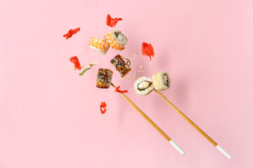 Tasty flying sushi rolls, ginger, cucumber and chopsticks on pink background