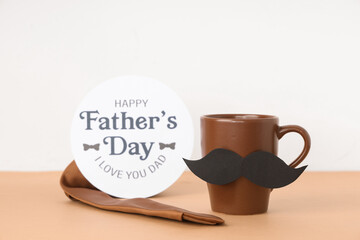 Cup with mustache, tie and paper with text HAPPY FATHER'S DAY on table against white background