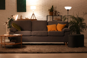 Interior of living room with glowing lamp, sofa and coffee table at evening