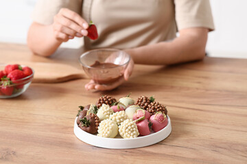 Young woman dipping fresh strawberry into bowl with melted chocolate at home, closeup