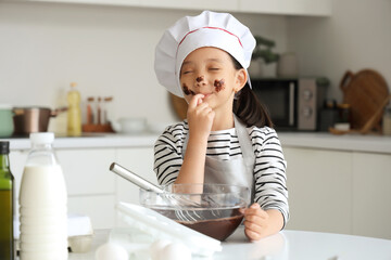 Funny little Asian girl eating melted chocolate in kitchen