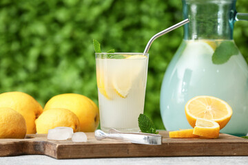 Glass and jug of fresh lemonade with mint on grey table outdoors