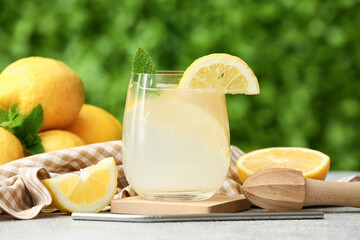 Glass of fresh lemonade with mint and juicer on grey table outdoors