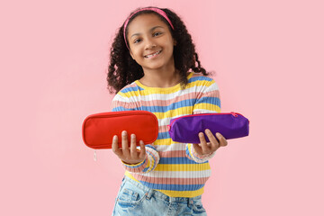 Little African-American girl with pencil cases on pink background