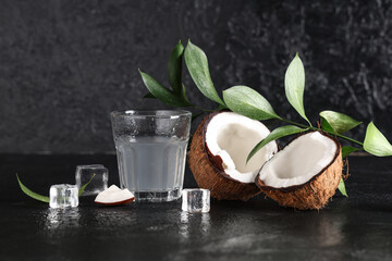 Halves of fresh coconut with glass of water and ice cubes on black background