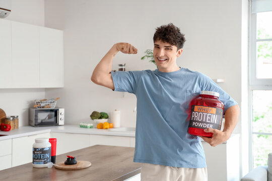 Sporty young man with protein powder showing muscles in kitchen