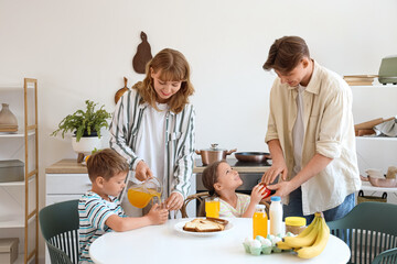 Little children with their parents having breakfast at table in kitchen