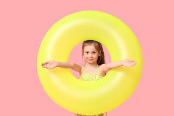 Cute little girl in swimsuit with inflatable ring on pink background