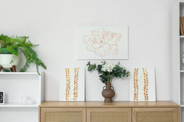 Vase with eucalyptus and stylish paintings on commode in living room