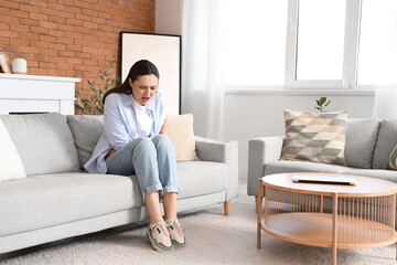 Young woman suffering from menstrual cramps on sofa at home