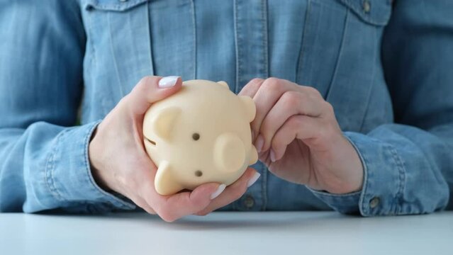 Person open and shaking coins out of piggy bank on a desk. Using last savings, unemployment and bankruptcy concept. Crisis and dismissal. Woman checking piggy box content