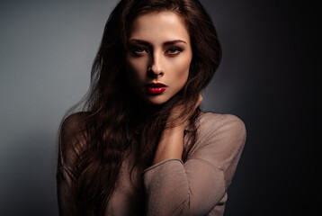 Sexy makeup with red lipstick woman holding long brown curly hair and posing in elegant dress with...