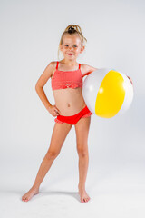 Blonde girl in red swimsuit holding a beach ball, standing casually with hand on hip