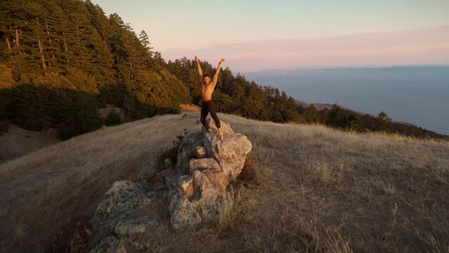 Male ballet dancer doing a choreographic dance move standing on a rock at sunset over looking the ocean in San Francisco.