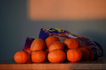 A bag of oranges sitting atop a table, illuminated by sunlight filtering through a nearby window