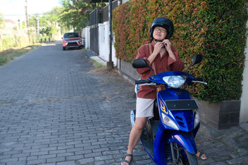 A woman sitting on a motorbike is taking off her helmet