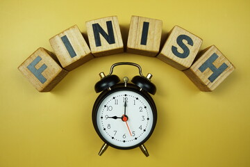 Finish word and alarm clock top view on yellow background