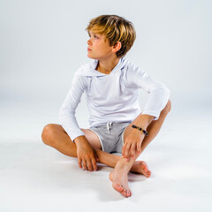 Youth male child in swim shorts and a hoodie sitting cross legged on the floor