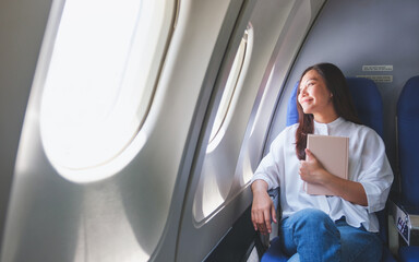 Portrait image of a woman holding book while traveling on an airplane