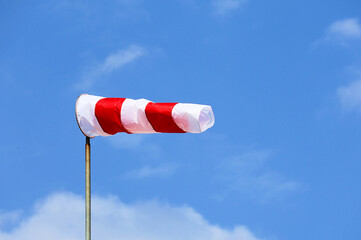 Windsock in red and white colors against a blue sky. Object to measure wind direction.