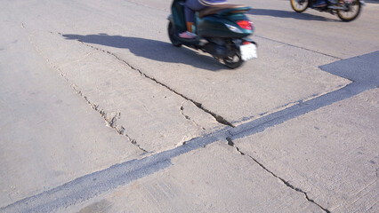 Blurred movement of 2 motorcycles on the old damaged concrete road with collapsed and long broken crack lines on surface