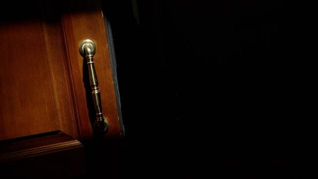 Hand gripping brass handle on partially opened wooden door, sunlight and shadows