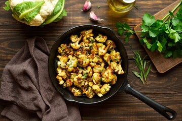 Roasted cauliflower in cast iron pan on wooden background